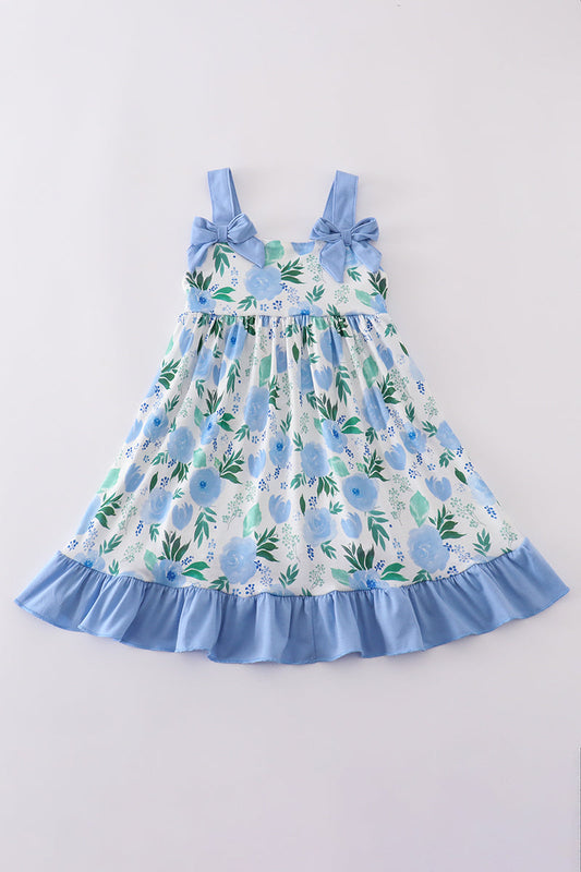 White dress with blue ruffled trim and blue straps with blue bows and blue flowers on dress