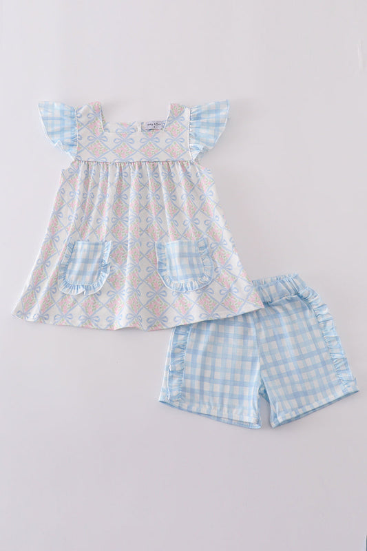 White top with pink flowers and blue bows and blue gingham shorts